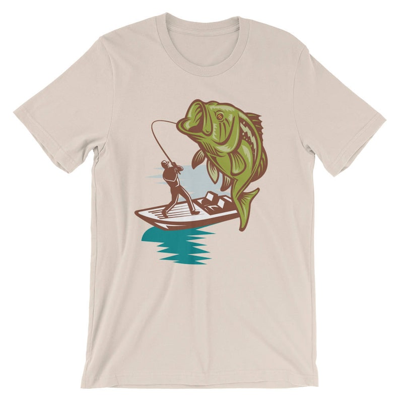 May include: A beige t-shirt with a graphic of a person fishing from a boat with a large bass jumping out of the water.