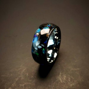 Puede incluir: Un anillo negro con una incrustaci&oacute;n azul y verde iridiscente. El anillo est&aacute; hecho de carburo de tungsteno y tiene un acabado pulido.