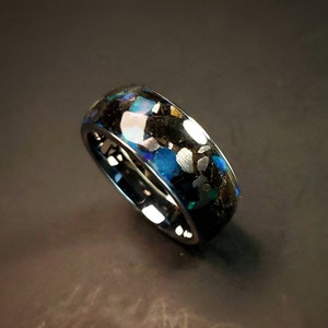 Puede incluir: Un anillo negro con una incrustaci&oacute;n azul y plateada. La incrustaci&oacute;n est&aacute; hecha de peque&ntilde;os trozos de material que est&aacute;n engastados en una resina.