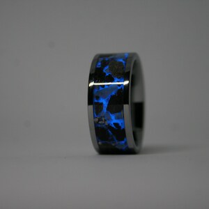 May include: A black tungsten ring with a blue glow-in-the-dark inlay. The inlay has a speckled pattern.