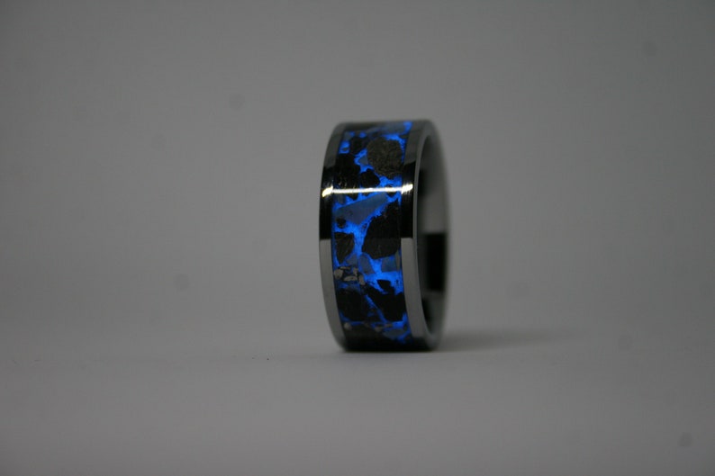 May include: A black tungsten ring with a blue glow-in-the-dark inlay. The inlay has a speckled pattern.