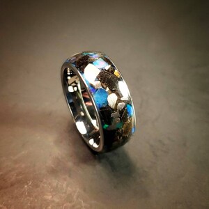 Puede incluir: Un anillo negro con una banda de virutas de &oacute;palo azul, verde y dorado iridiscentes.
