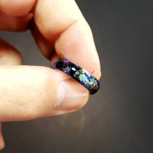 May include: A silver ring with a black band and a colorful inlay of iridescent opal, black, and gold glitter.