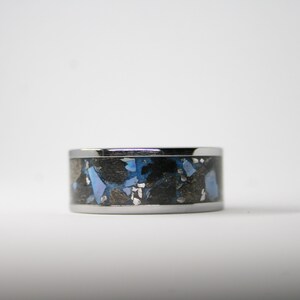 May include: A silver ring with a black and blue inlay. The inlay is made of small pieces of material that are randomly arranged.