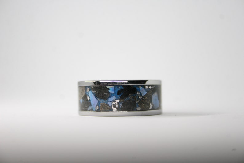 May include: A silver ring with a black and blue inlay. The inlay is made of small pieces of material that are randomly arranged.