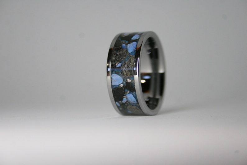 May include: A silver ring with a black and blue inlay. The inlay has a speckled pattern of blue and black.