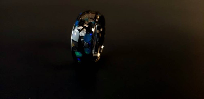 Puede incluir: Un anillo negro con una incrustaci&oacute;n azul y blanca. La incrustaci&oacute;n est&aacute; hecha de peque&ntilde;as piezas irregulares de material que est&aacute;n engastadas en el metal negro.
