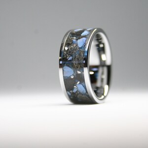 May include: A silver ring with a blue and black inlay. The inlay is made of a material that looks like crushed stone.