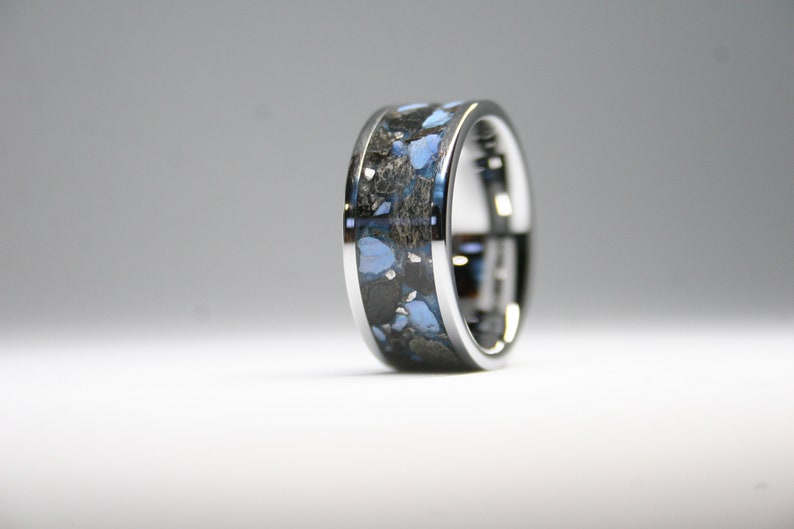 May include: A silver ring with a blue and black inlay. The inlay is made of a material that looks like crushed stone.