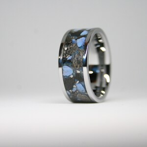 May include: A silver ring with a black and blue inlay. The inlay has a speckled pattern of blue and black.