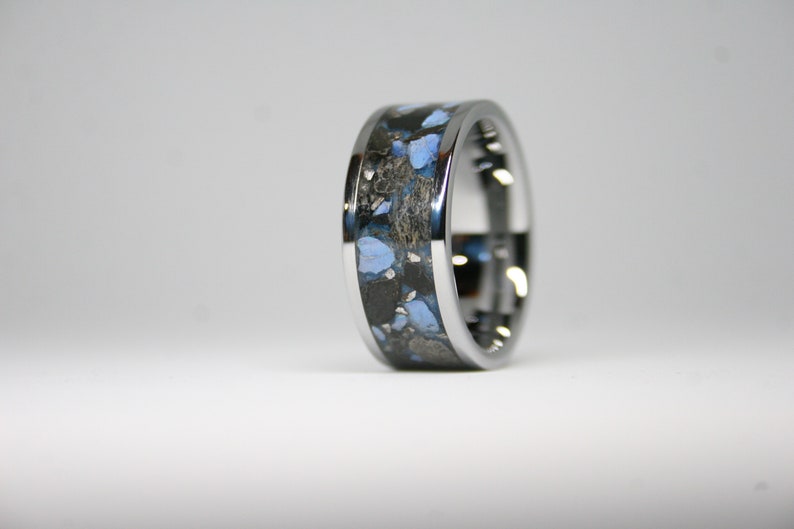 May include: A silver ring with a black and blue inlay. The inlay has a speckled pattern of blue and black.