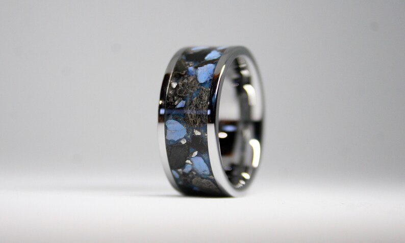 May include: A silver ring with a black and blue inlay. The inlay is made of a mixture of materials, including blue and black stones.
