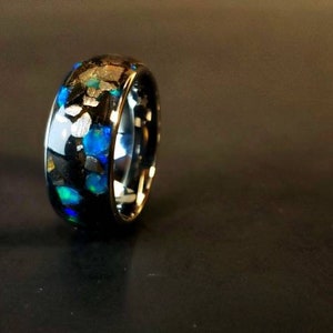 Puede incluir: Un anillo negro con motas azules y plateadas incrustadas en la banda.