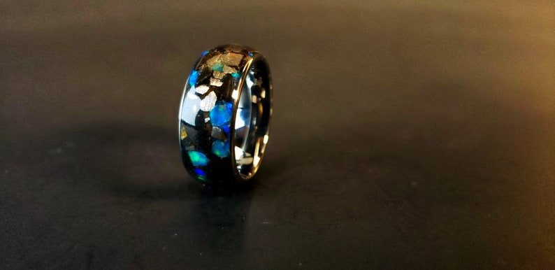 Puede incluir: Un anillo negro con motas azules y plateadas incrustadas en la banda.