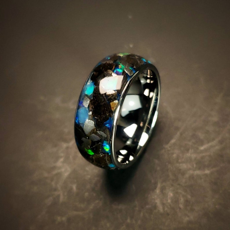 Puede incluir: Un anillo de tungsteno negro con una banda de incrustaciones de &oacute;palo azul, verde y blanco iridiscente.