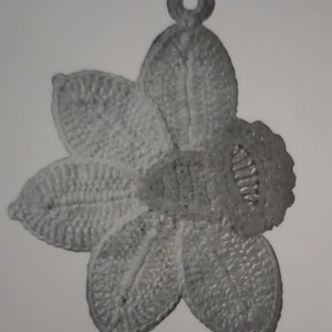 May include: A crocheted daffodil flower with a loop at the top, perfect for a charm or embellishment. The flower is white and has a detailed design.