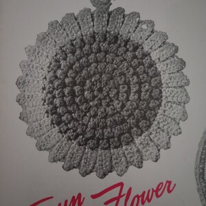 May include: A crocheted sunflower pot holder with a gray and white color scheme. The pot holder has a loop at the top for hanging.