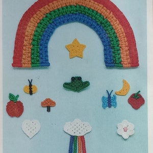 Op de afbeelding: Een regenboog-applicatie van gehaakt werk met een verscheidenheid aan andere gehaakte applicaties, waaronder een ster, een kikker, een vlinder, een paddenstoel, een hart, een wolk met een regenboog, een bloem, een halve maan en twee aardbeien.