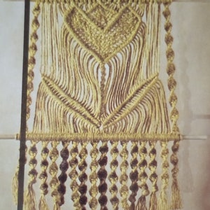 May include: A macrame wall hanging with a tulip design. The hanging is made of natural colored cord and has a fringe at the bottom. The text "TULIP TIE-UP" is printed below the hanging.