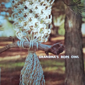 May include: A white rope owl with brown pine cones for eyes, hanging from a branch. The owl has a long, blue and brown tassel hanging from its body. The text "GRANDMA'S ROPE OWL" is printed below the owl.