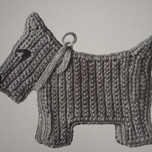 May include: A gray crocheted dog toy with a loop for hanging. The dog is in a standing position with its head turned to the left.