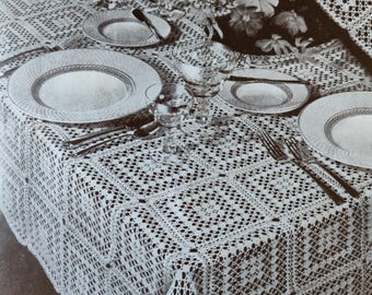 May include: A white crocheted tablecloth with a repeating square pattern. The tablecloth is set for a formal dinner with plates, silverware, and glasses.
