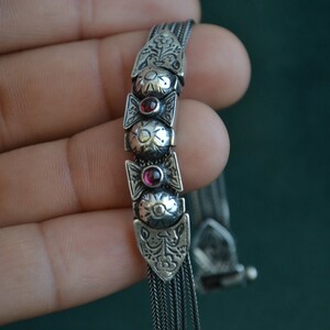 May include: A silver bracelet with a chain design and three red gemstone accents.
