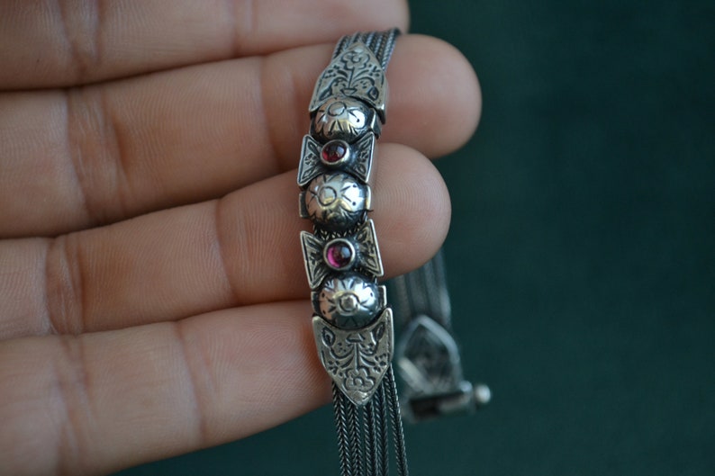 May include: A silver bracelet with a chain design and three red gemstone accents.