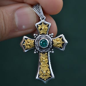 May include: A silver and gold cross pendant with an ornate design and a green gemstone in the centre.