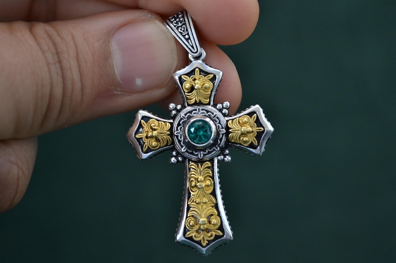 May include: A silver and gold cross pendant with an ornate design and a green gemstone in the centre.
