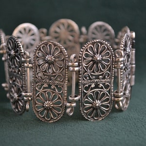 Puede incluir: Pulsera de filigrana plateada con un dise&ntilde;o calado. La pulsera presenta eslabones ovalados con motivos florales y bisagras de conexi&oacute;n. El intrincado trabajo en metal crea una apariencia delicada y ornamentada, adecuada para joyer&iacute;a.