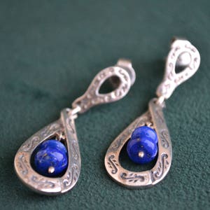 以下が含まれることがあります： 複雑なデザインと青い宝石のアクセントが付いた銀のイヤリングのペア
