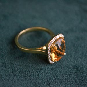 Pode incluir: Um anel de ouro com uma grande pedra de top&aacute;zio de forma quadrada cercada por um halo de diamantes menores.