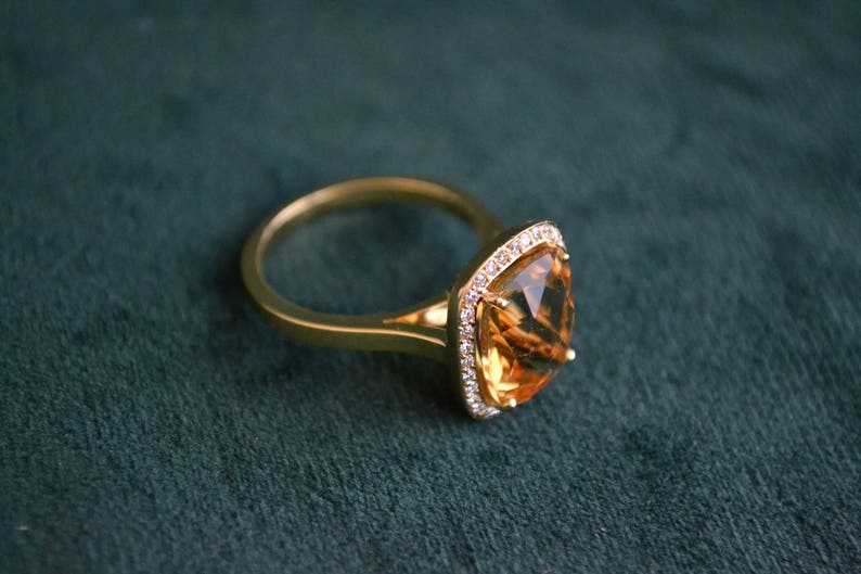 Pode incluir: Um anel de ouro com uma grande pedra de top&aacute;zio de forma quadrada cercada por um halo de diamantes menores.