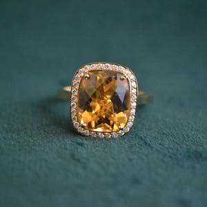 Pode incluir: Um anel de ouro com uma grande pedra de top&aacute;zio de corte almofada rodeada por um halo de diamantes menores.