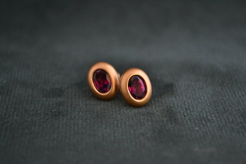 Puede incluir: Un par de pendientes ovalados con engaste de oro rosa y una piedra preciosa roja oscura.