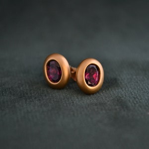 Puede incluir: Un par de pendientes de bot&oacute;n de oro con una piedra ovalada de color rojo oscuro en cada uno.