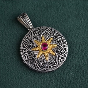 Peut inclure: Un pendentif en argent avec un motif d'étoile dorée et une pierre précieuse rose au centre. Le pendentif est entouré de motifs floraux complexes.