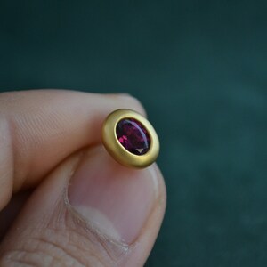 Puede incluir: Un pendiente de oro con una piedra ovalada de color rojo oscuro.