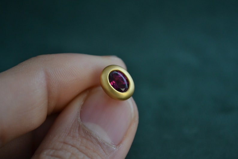 Puede incluir: Un pendiente de oro con una piedra ovalada de color rojo oscuro.