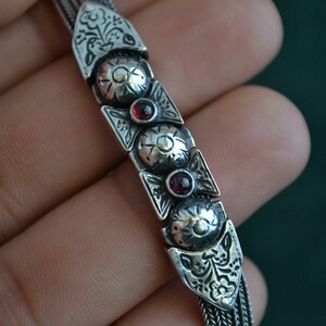 May include: A silver chain bracelet with intricate floral designs and three red gemstones.
