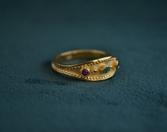 May include: A gold ring with three gemstones: a ruby, an emerald, and a smaller black stone. The ring has a textured band.