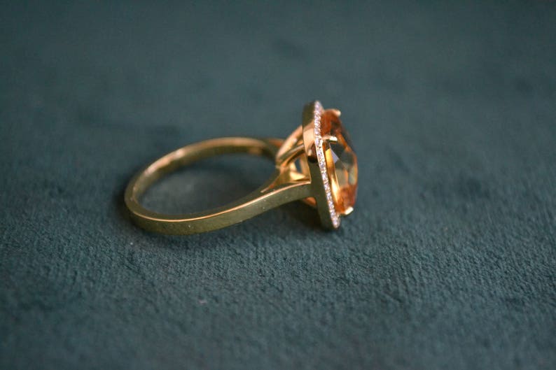 Pode incluir: Um anel de ouro com uma grande gema laranja facetada cercada por gemas menores e transparentes.