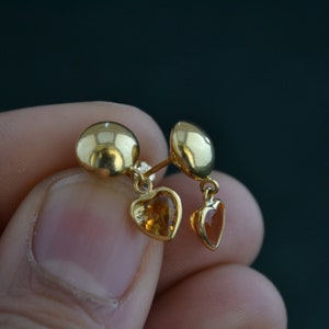 Puede incluir: Pendientes de bot&oacute;n dorados con colgantes en forma de coraz&oacute;n. Los pendientes presentan un bot&oacute;n redondo y una peque&ntilde;a gema en forma de coraz&oacute;n. Las gemas son de color &aacute;mbar c&aacute;lido. Los pendientes se sostienen.