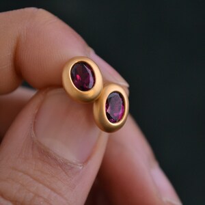Puede incluir: Un par de pendientes de bot&oacute;n de oro con piedras redondas de color rojo oscuro.