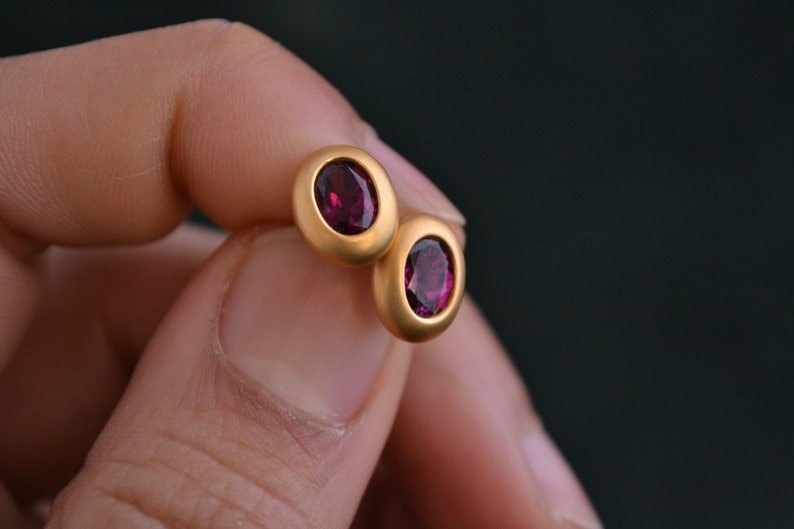 Puede incluir: Un par de pendientes de bot&oacute;n de oro con piedras redondas de color rojo oscuro.