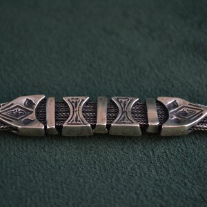 May include: A silver chain bracelet with a decorative clasp. The clasp is made of several interlocking pieces with intricate designs.