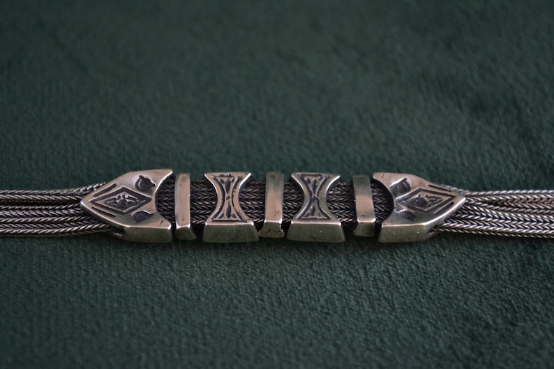 May include: A silver chain bracelet with a decorative clasp. The clasp is made of several interlocking pieces with intricate designs.