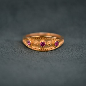 May include: A gold ring with three pink gemstones set in a decorative band.