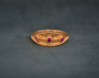 May include: A gold ring with three pink gemstones set in a decorative band.
